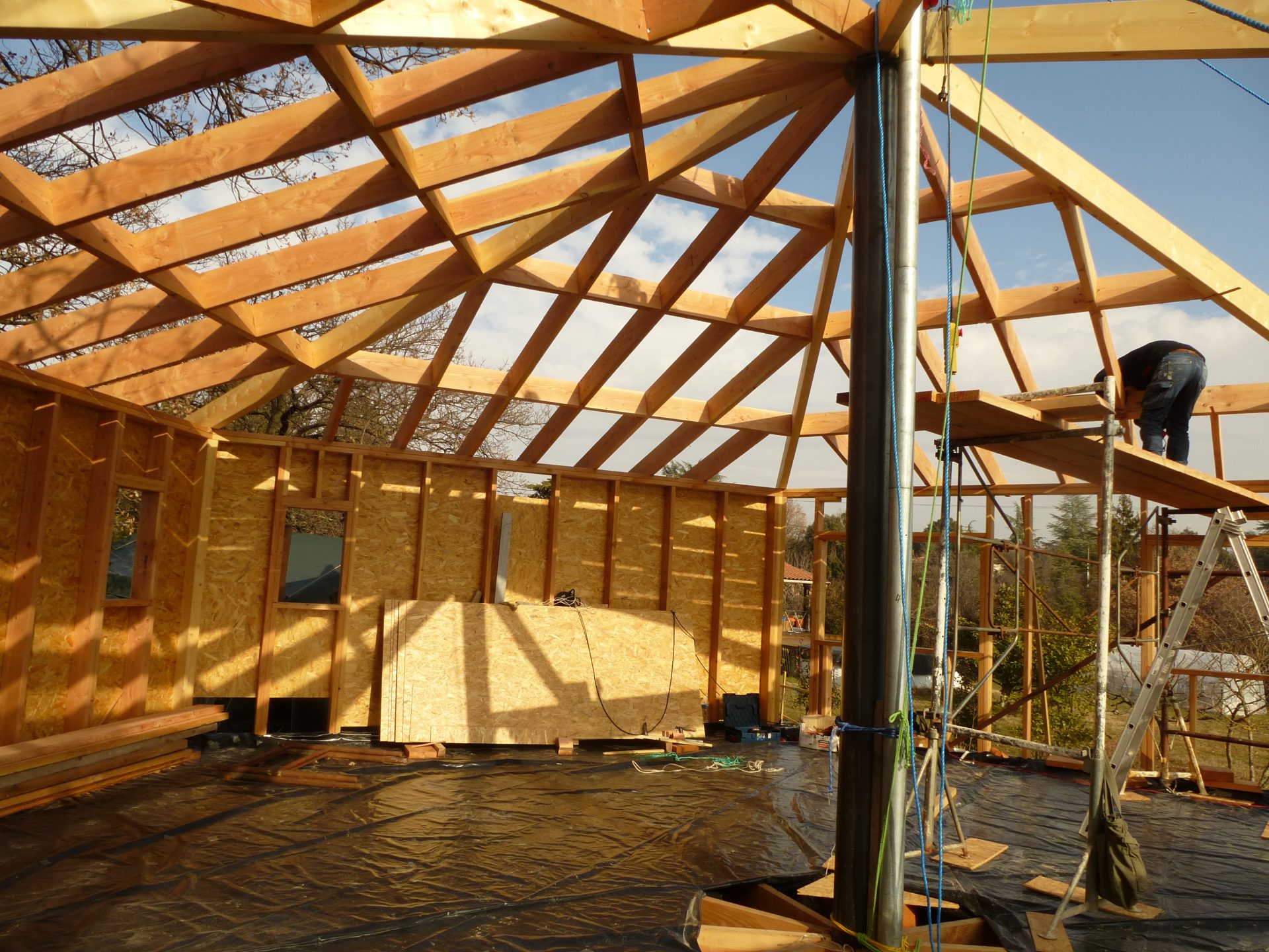 Charpente en bois clair montée à nu contre le ciel, chevrons et pannes visibles.