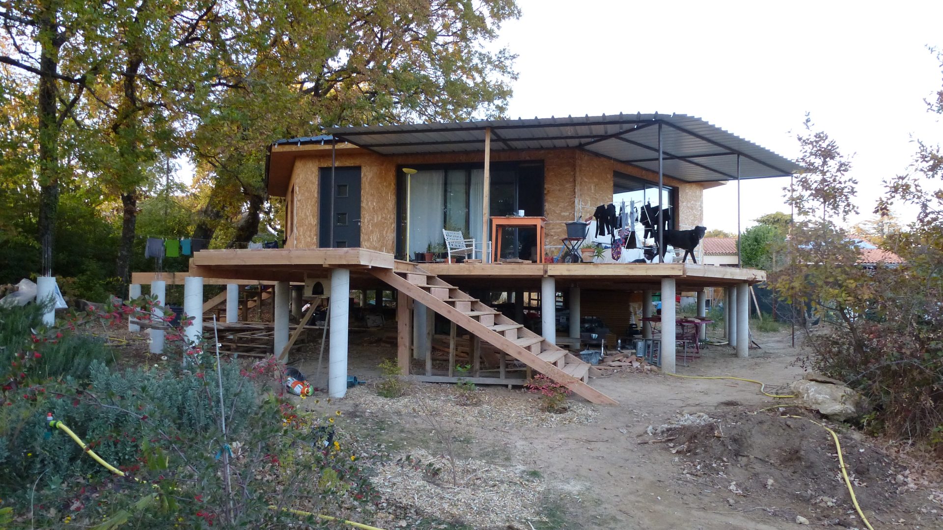 La maison vue depuis le jardin, avec sa terrasse sur pilotis et l'escalier extérieur qui y monte.