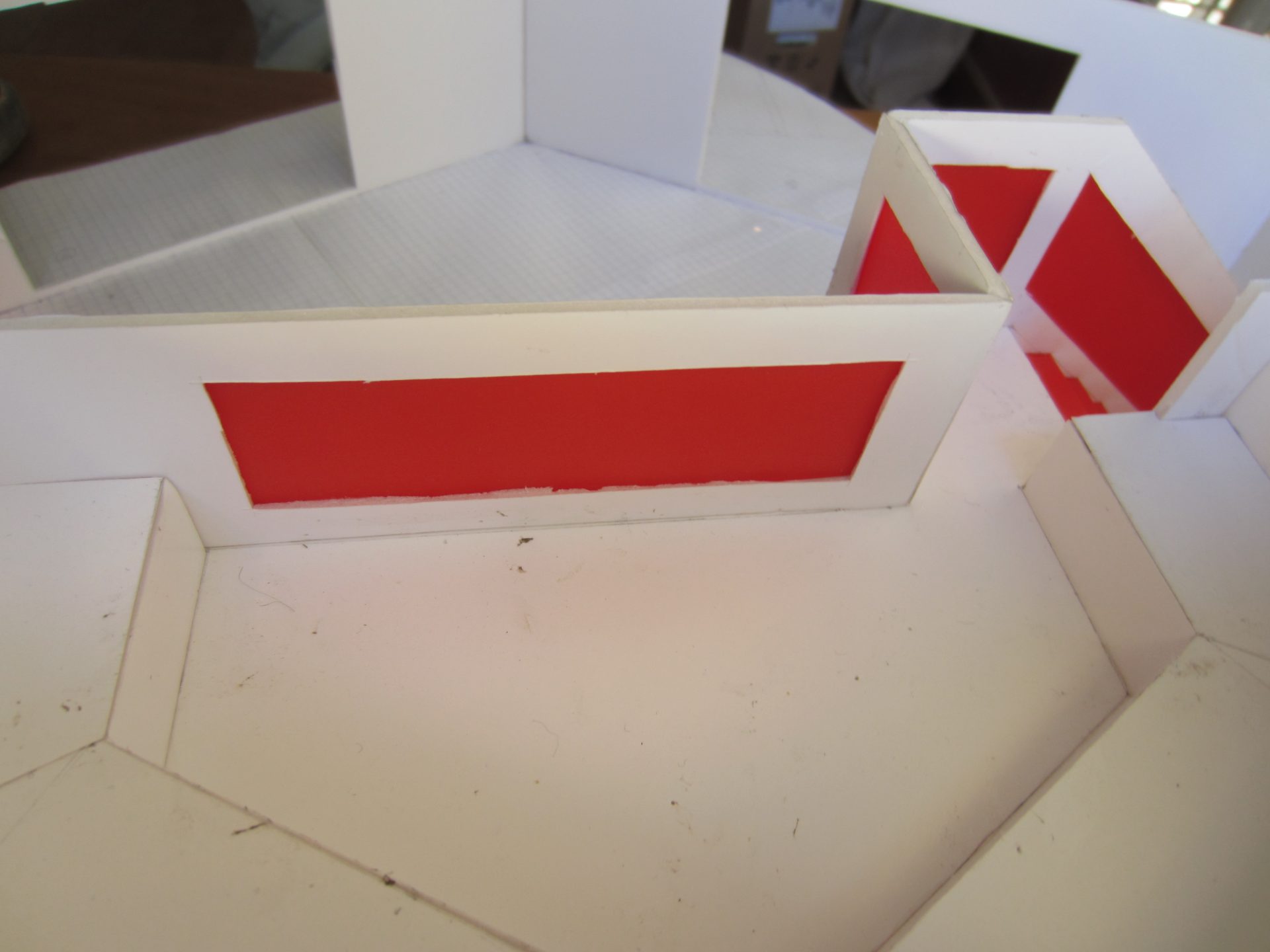 Vue intérieure de la maquette : un large bandeau rouge court sous le rampant du toit, au-dessus des cloisons blanches.