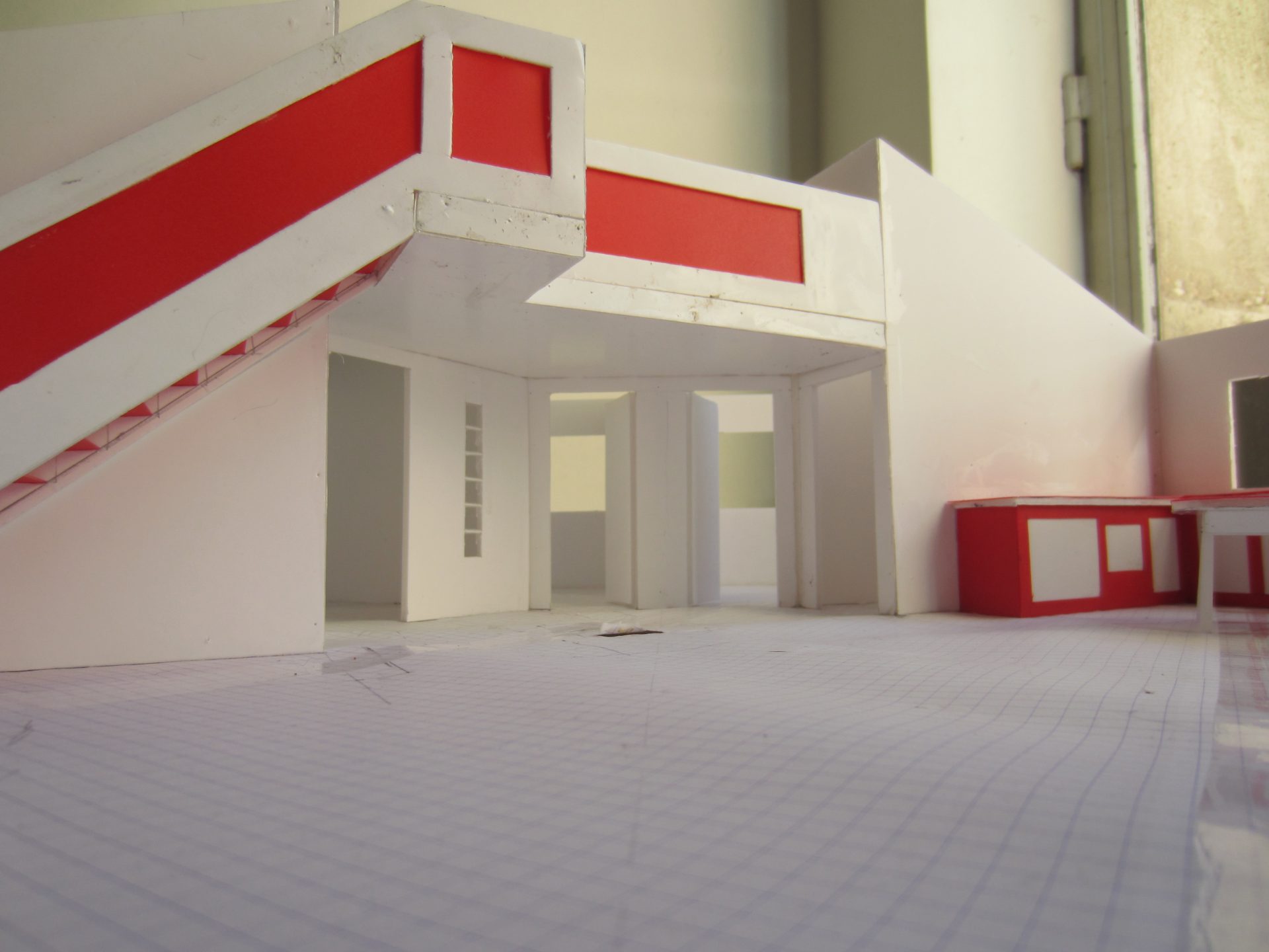 Perspective intérieure de la maquette, la lumière du jour entrant par une ouverture et éclairant le bandeau rouge.
