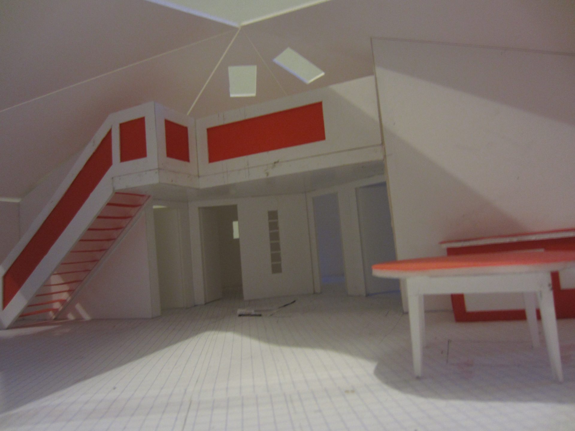 La plus large des vues intérieures de la maquette : le volume complet, l'escalier rouge, le bandeau et une table à plateau rouge au premier plan.